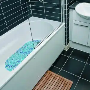 white bathtub with the blue flower shower mat, dark tiles, and bathroom mat