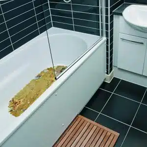 white bathtub with yellow shower mat, dark tiles, and bathroom mat